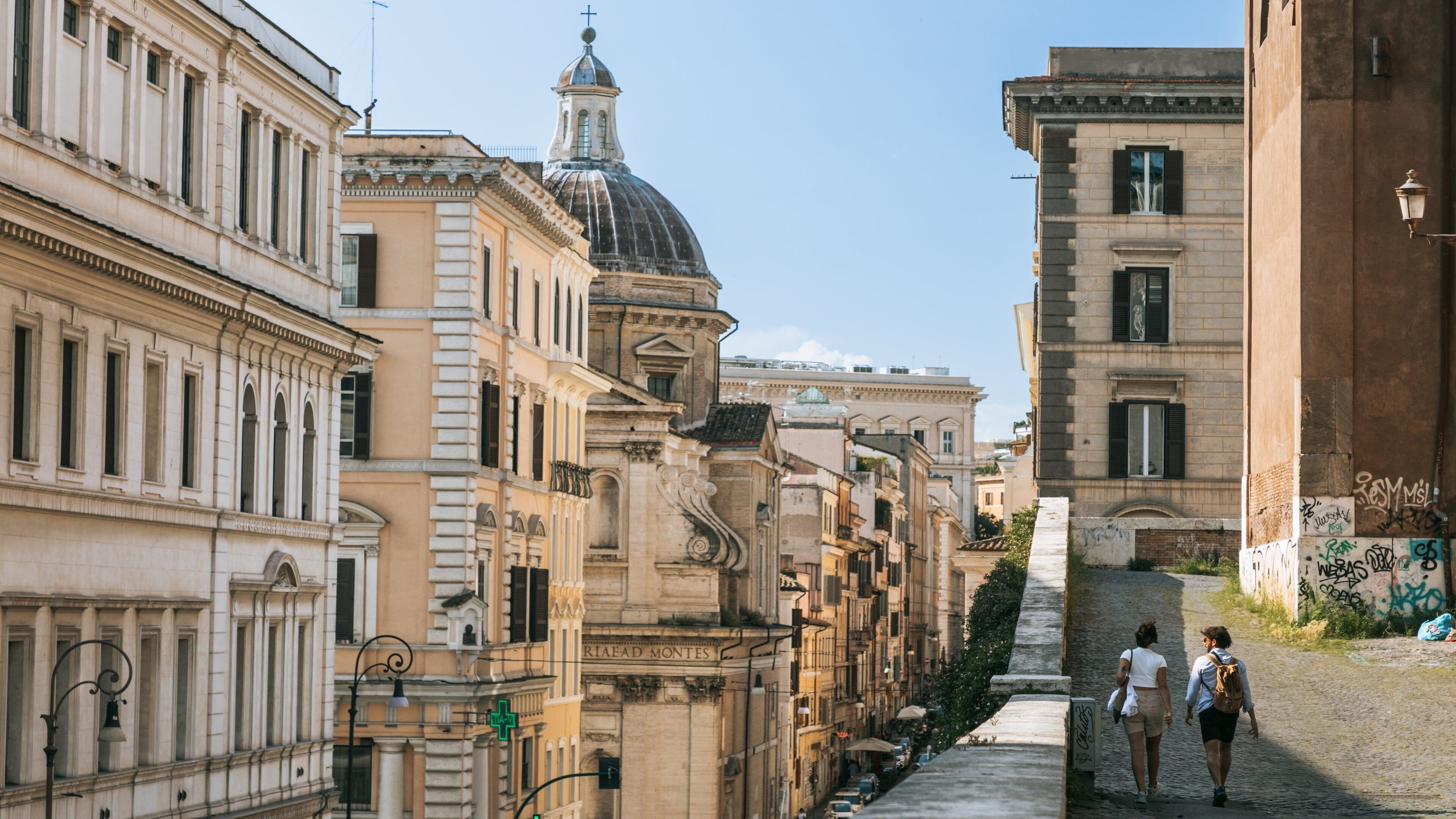 Una calle estrecha bordeada por edificios históricos de arquitectura clásica, que incluyen una cúpula destacada y una estatua.