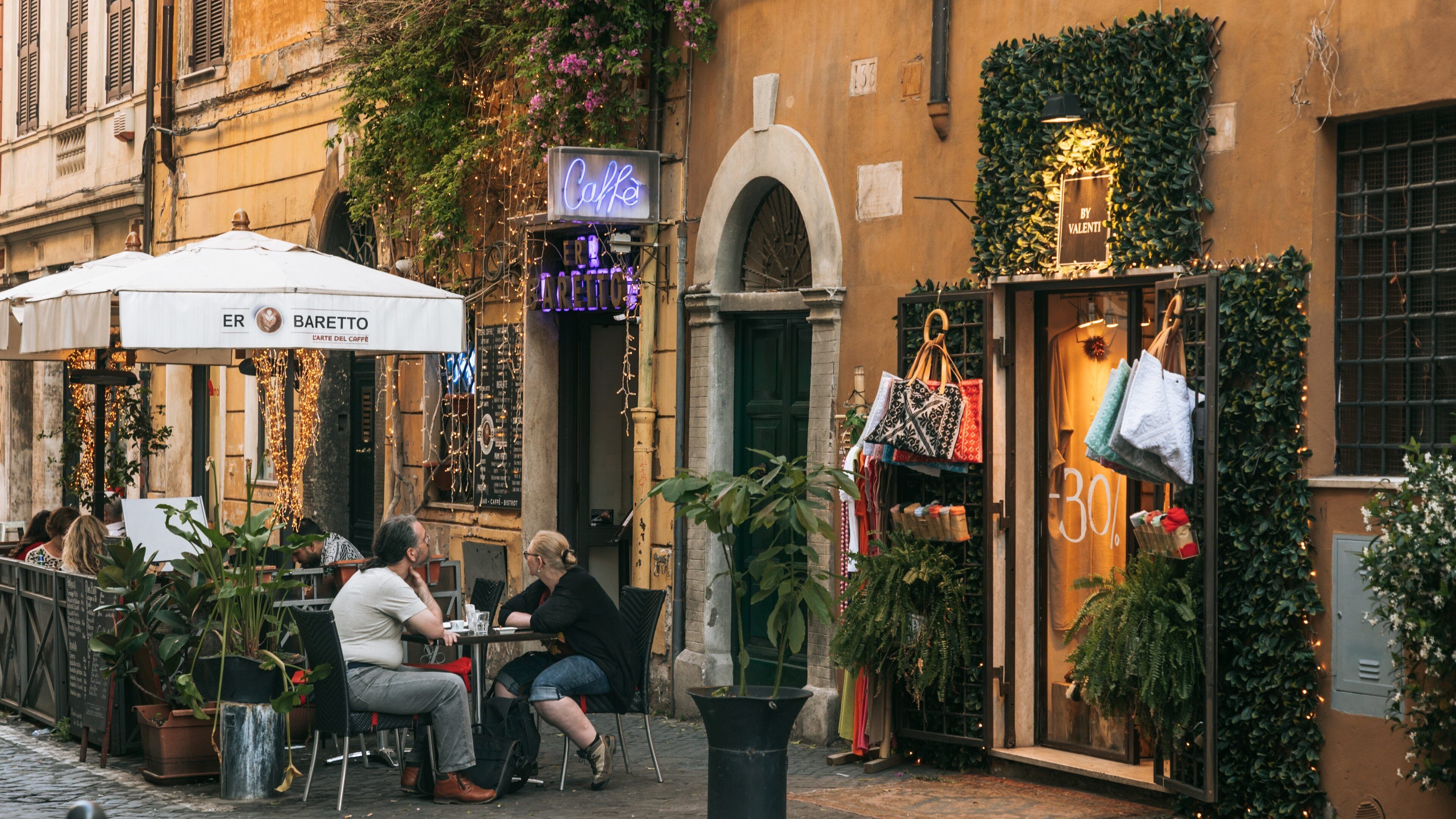Un café con terraza, un letrero de neón y una tienda de bolsos.