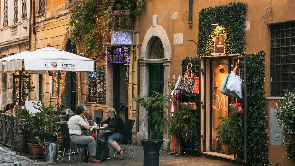 Un café con terraza, un letrero de neón y una tienda de bolsos.