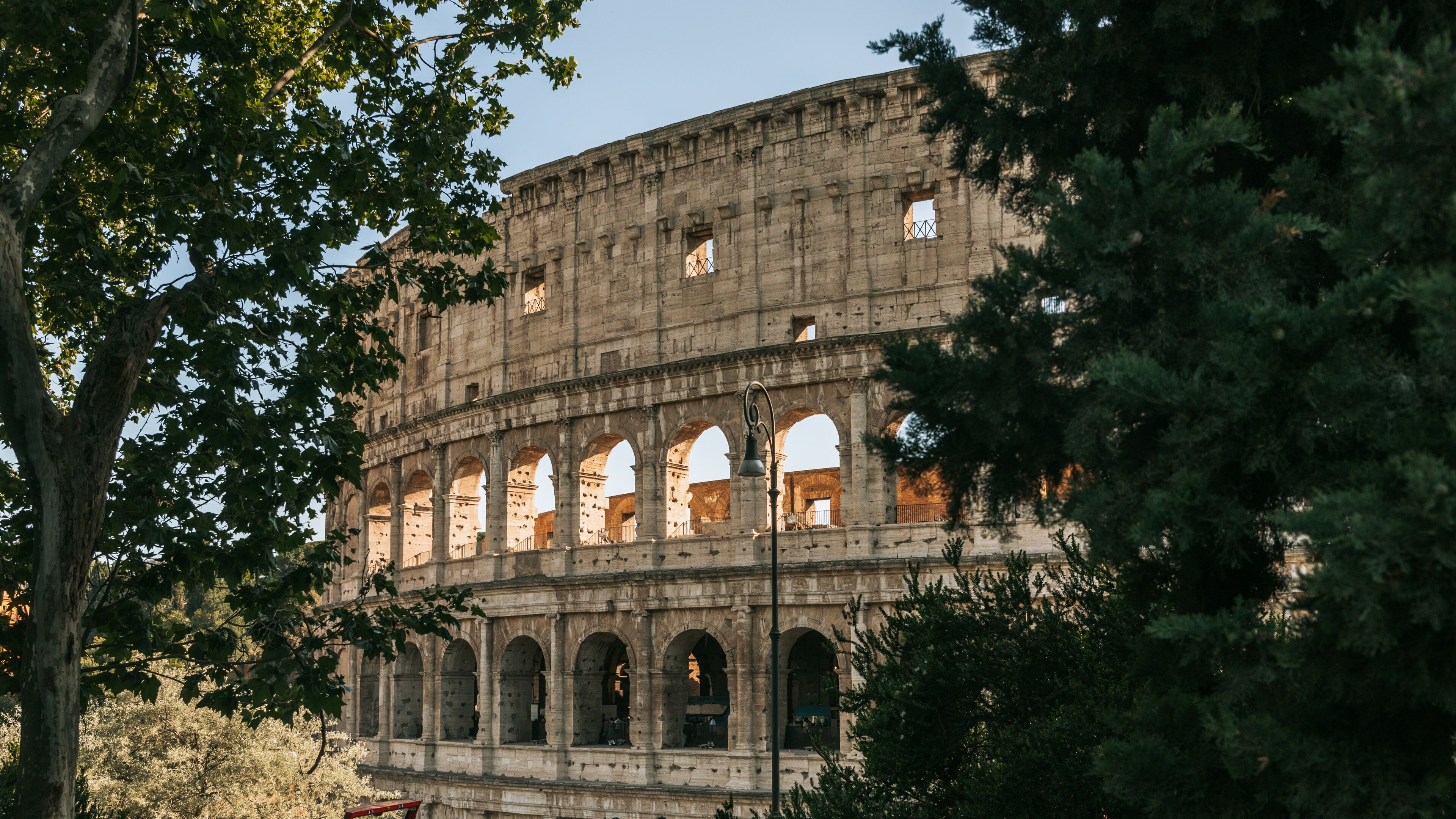 O Coliseu em Roma, Itália, parcialmente escondido por árvores.