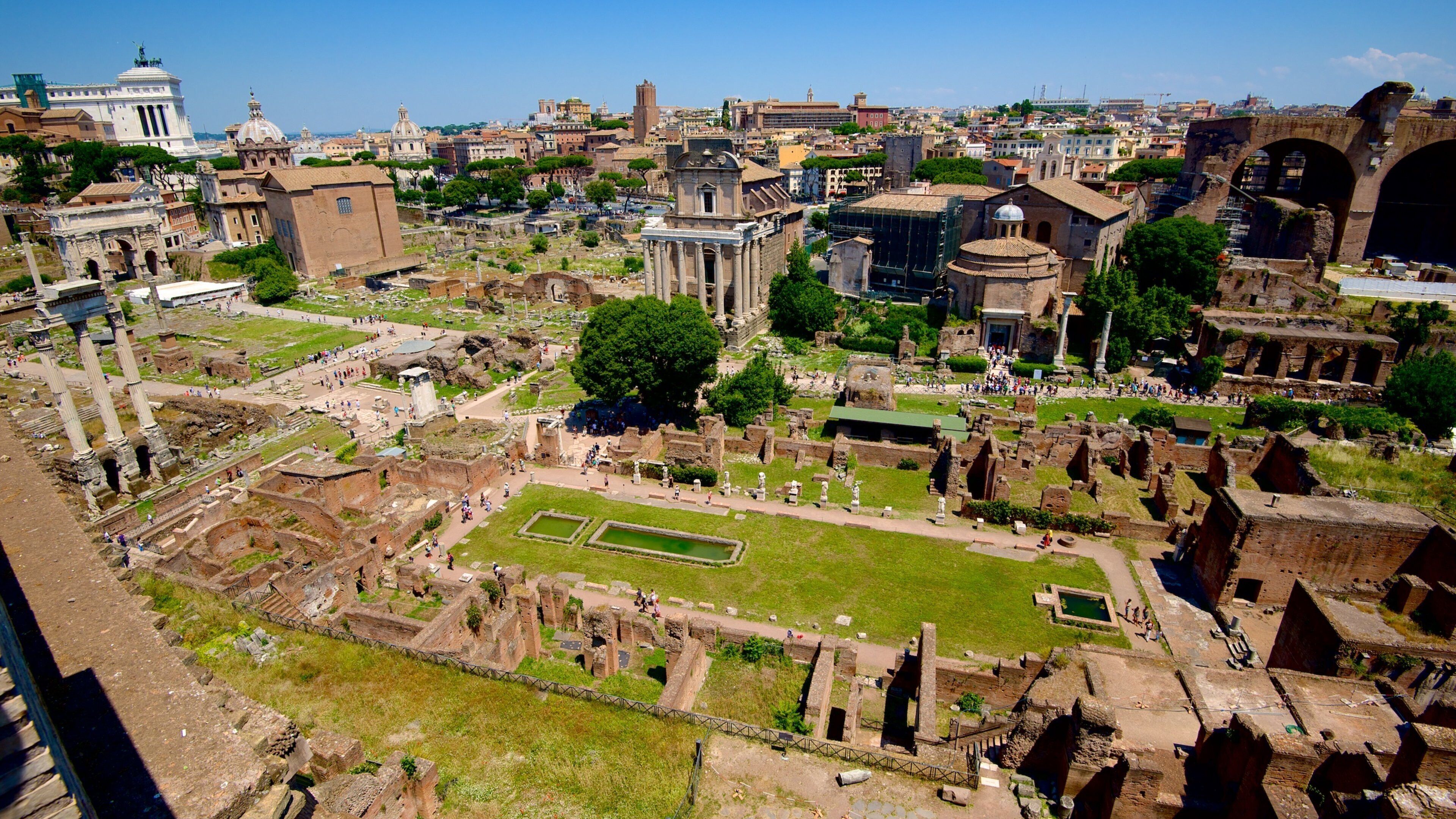 Ruinas antiguas con columnas y un espacio central abierto, rodeado de edificios históricos y una gran cúpula.
