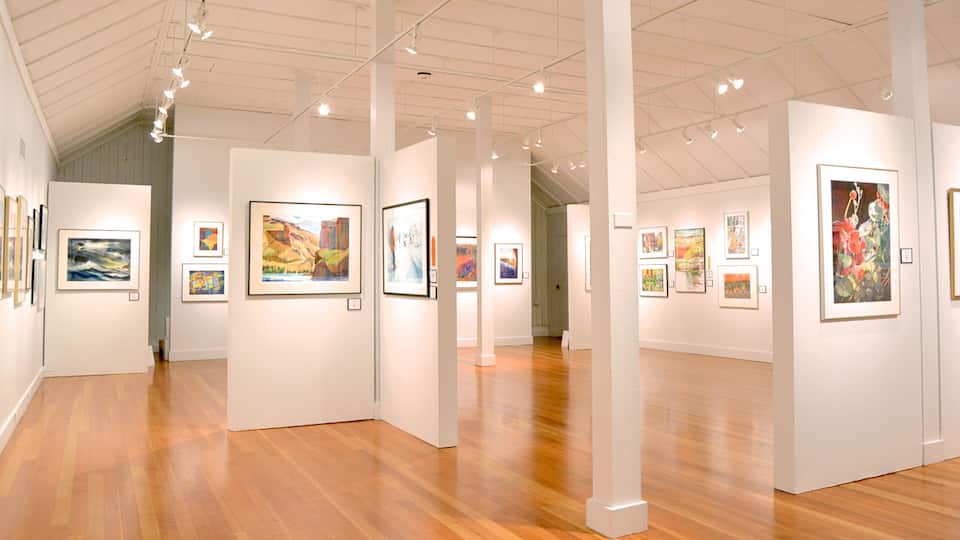 An art gallery with wooden floors and white walls, displaying various paintings.