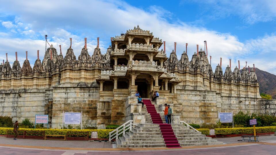 A large, ornate temple with intricate carvings and a central tower, surrounded by a well-maintained garden and a clear sky.