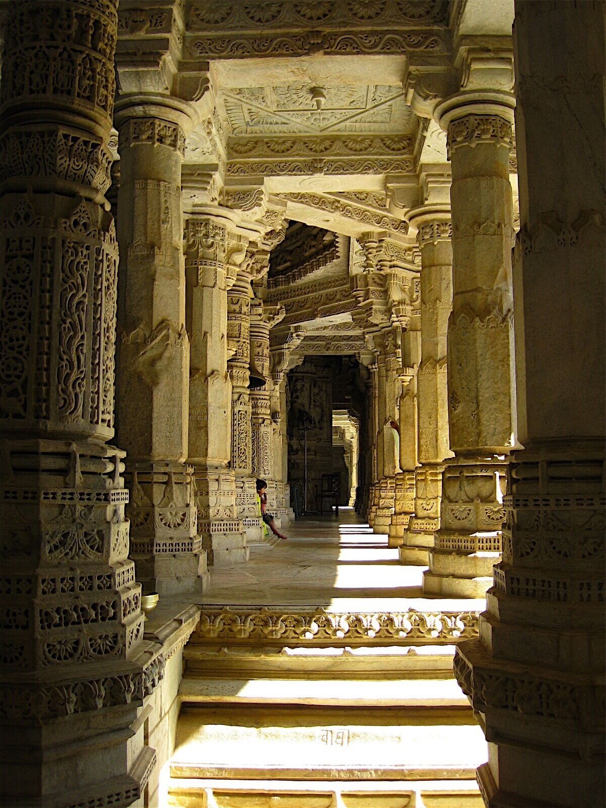An ornate corridor with intricate carvings and columns, leading to a darkened area.