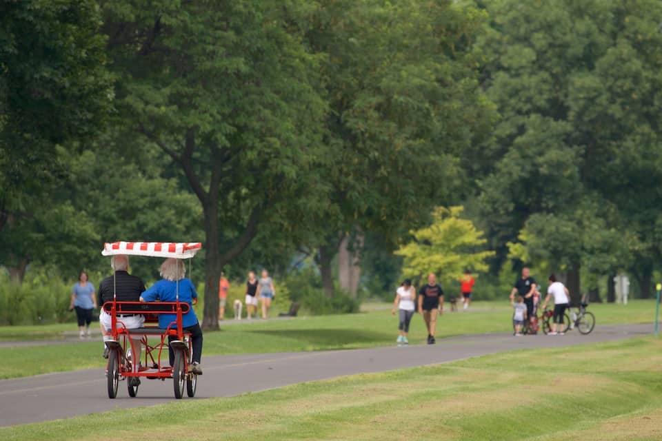 A park with a red and white striped cart, people walking, and trees.