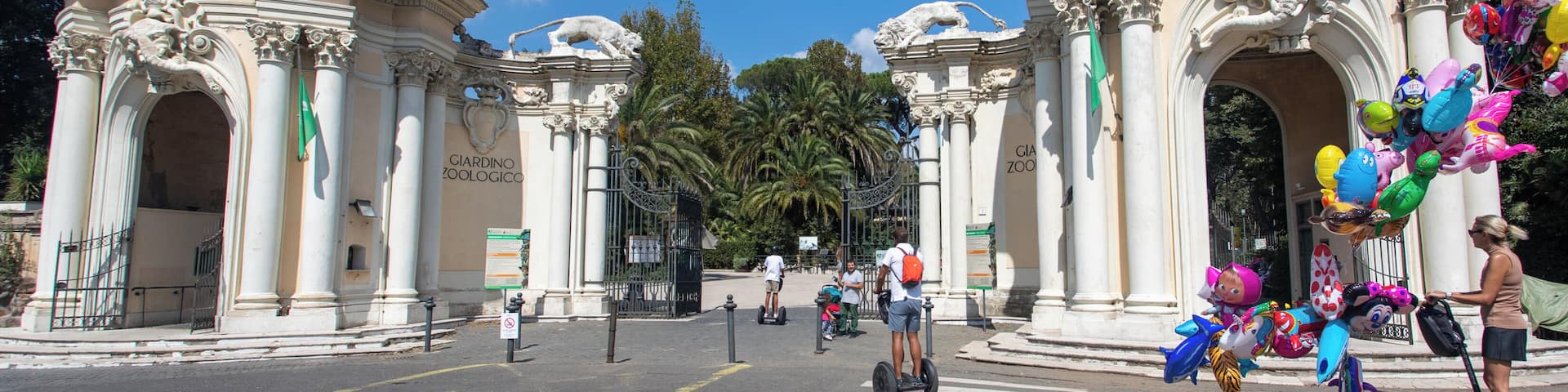 A historic entrance with ornate statues and columns, a crosswalk, and a person with a Segway.