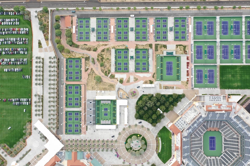 An aerial view of a sports complex with multiple tennis courts, parking areas, and landscaped gardens.