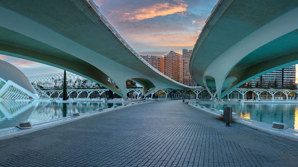 A modern architectural bridge with a reflective pool in the foreground.