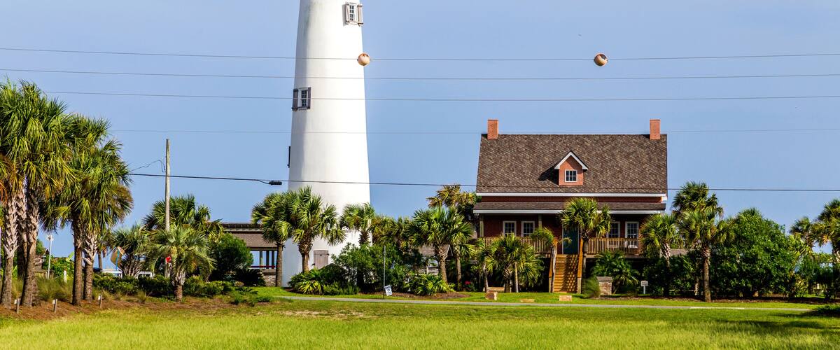 A lighthouse, a house, and palm trees.