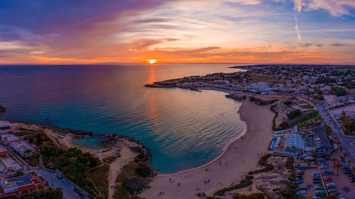 A coastal town at sunset with a beach, a pier, and a clear sky.