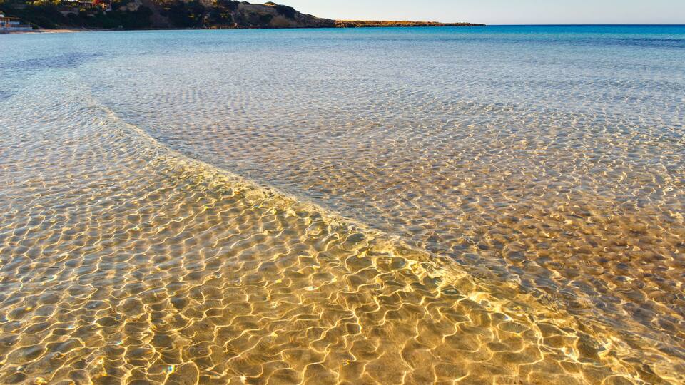 A clear beach with shallow water and a distant shoreline.