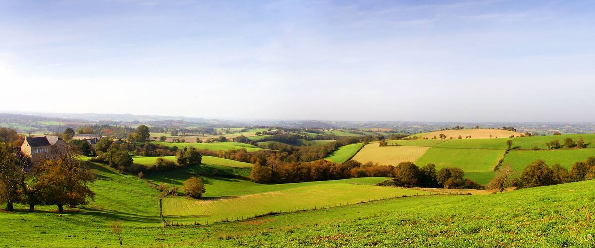 Rolling green hills, a distant village, and a prominent stone structure.