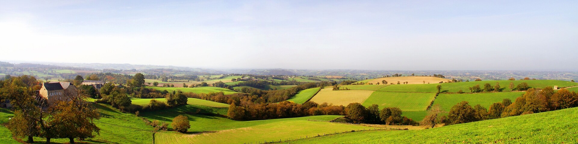 Rolling green hills, a distant village, and a prominent stone structure.