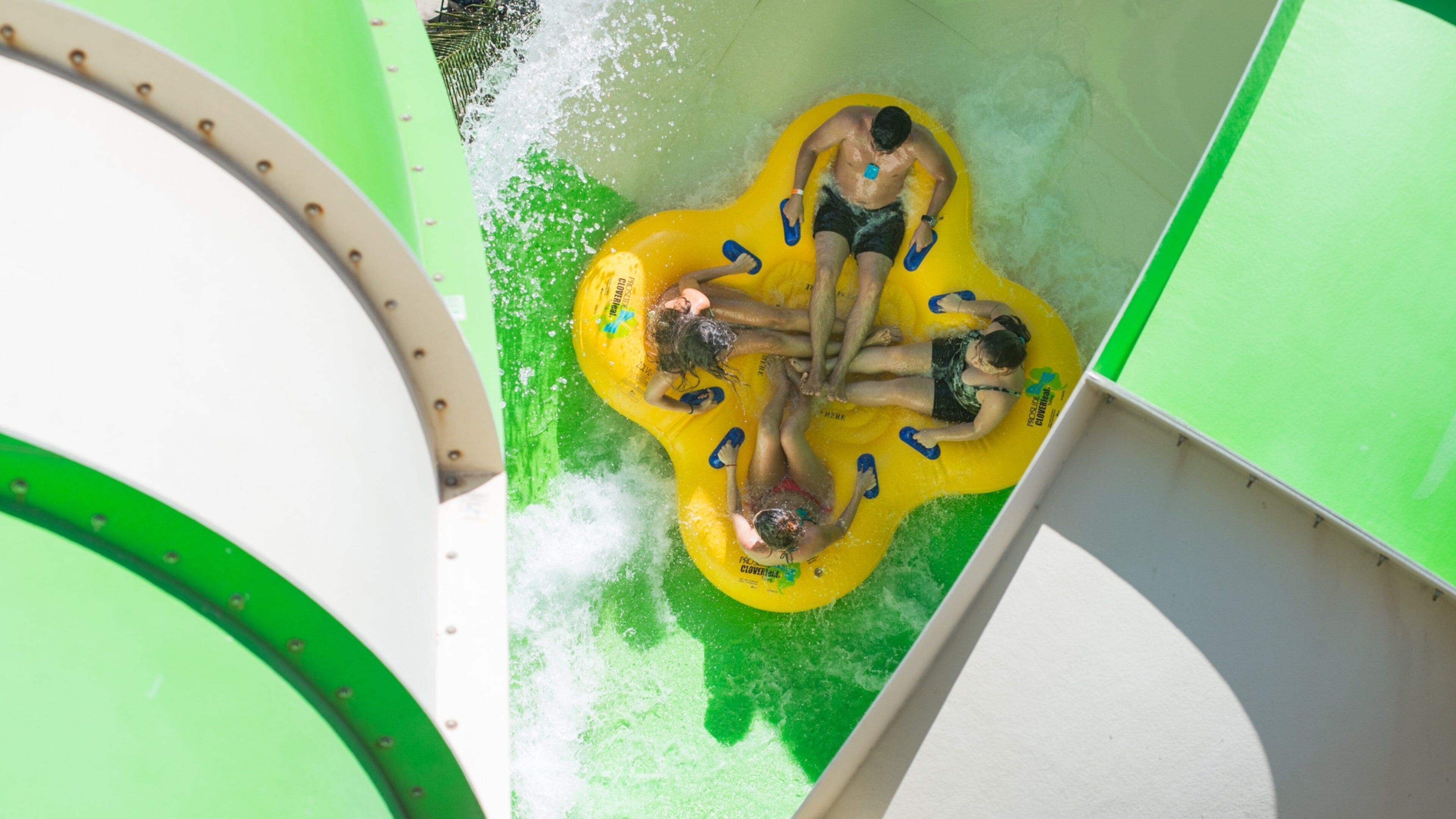 Un toboggan aquatique avec un radeau gonflable jaune et des structures vertes et blanches.