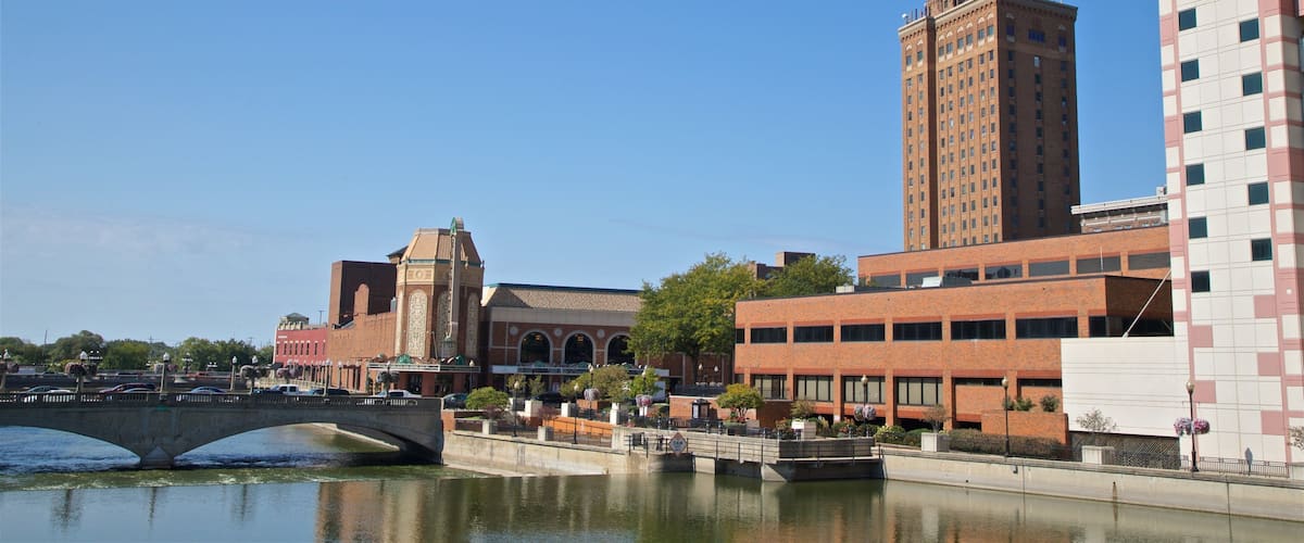 A cityscape with a bridge over a river, a historic building with arches, and modern high-rise buildings.