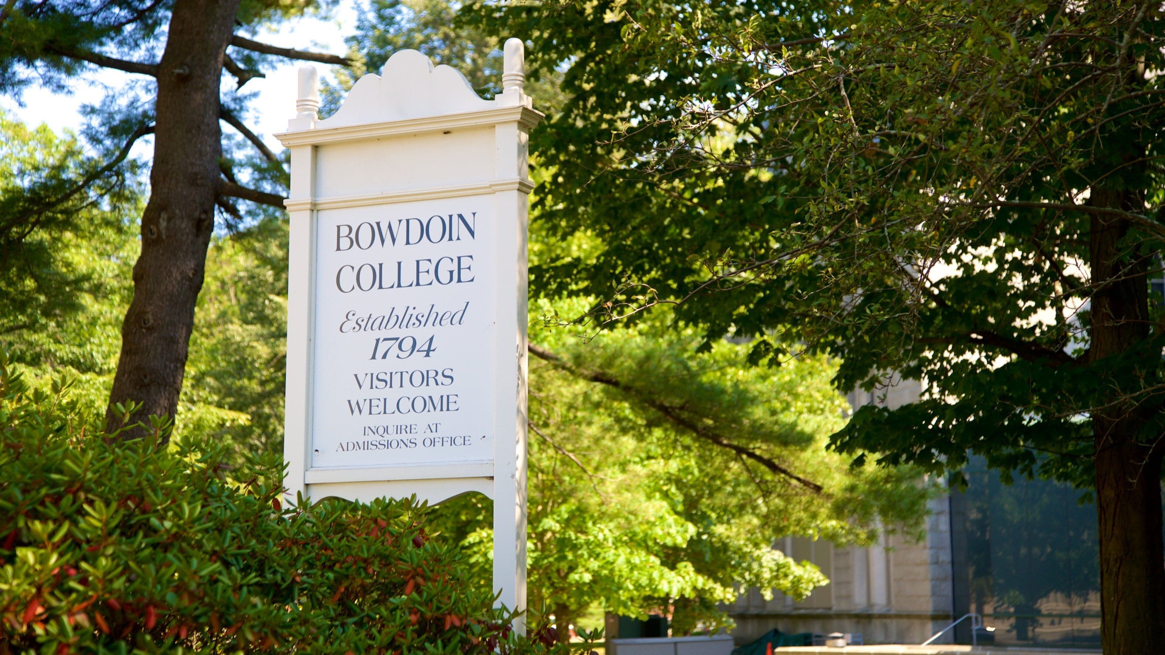 Schild von Bowdoin College mit Baum und Grünpflanzen im Hintergrund.