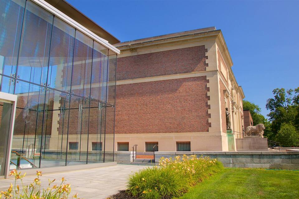 A modern building with glass facade and brick walls, surrounded by greenery and a statue.