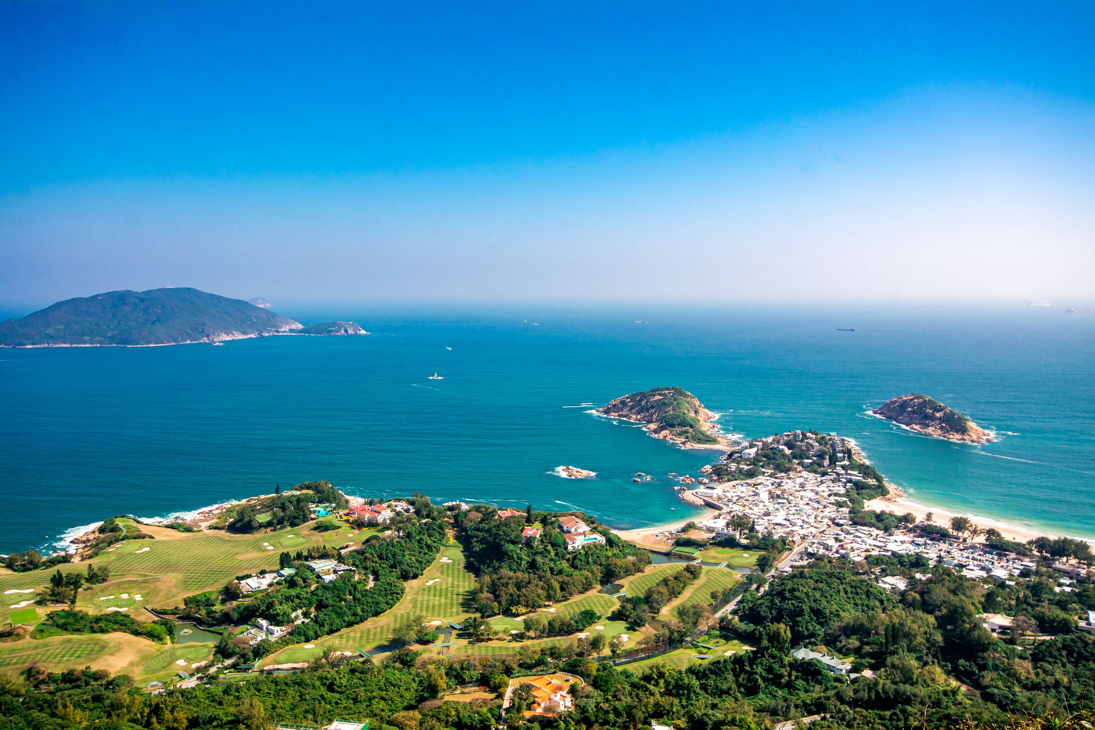 A coastal landscape with a golf course, a small town, and a large island in the distance.