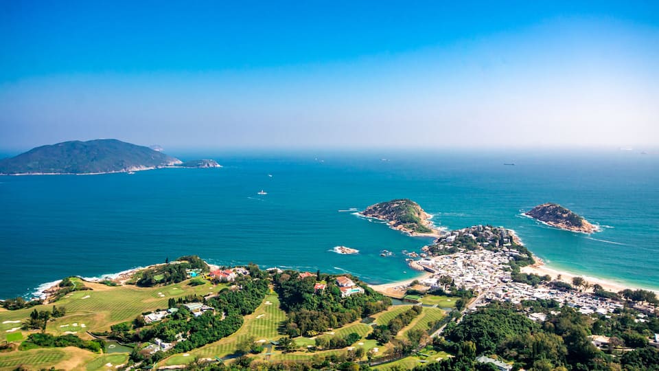 A coastal landscape with a golf course, a small town, and a large island in the distance.