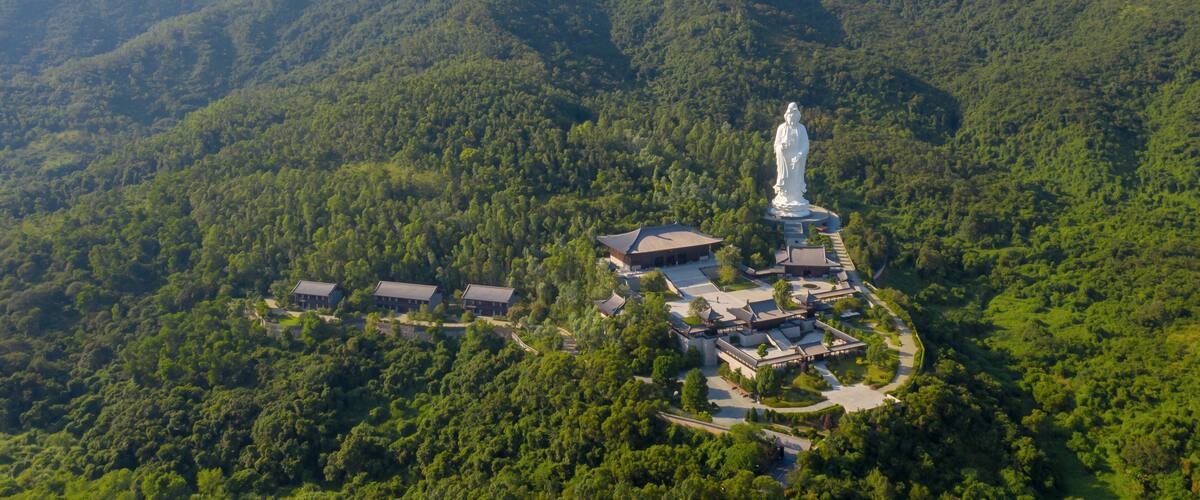 A statue surrounded by buildings and lush green mountains.