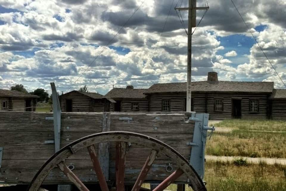 A wooden wagon wheel, a wooden fence, and a row of wooden houses under a cloudy sky.