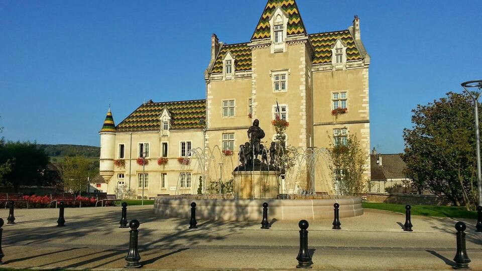 A large, historic building with a tower and a statue in front.