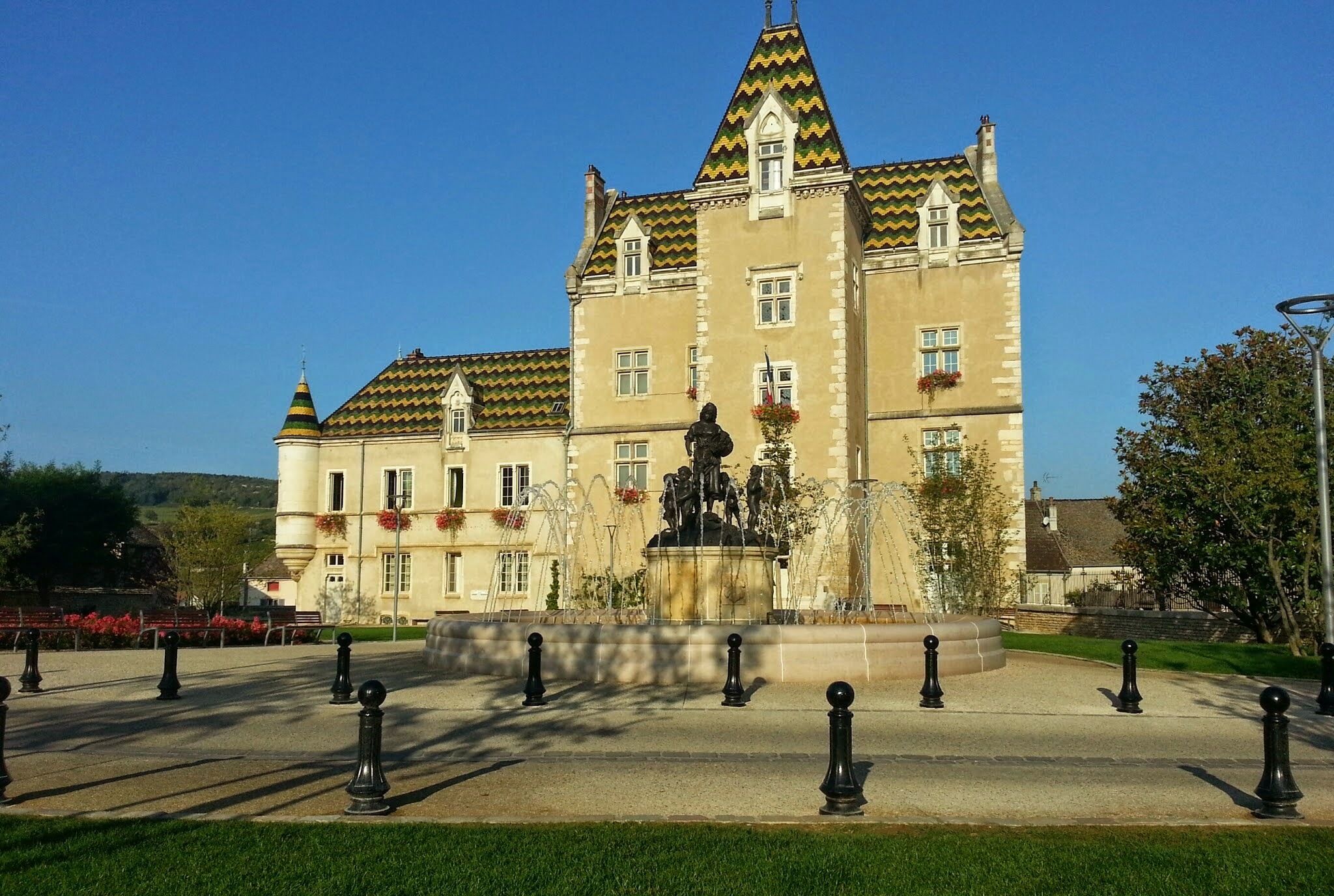 A large, historic building with a tower and a statue in front.