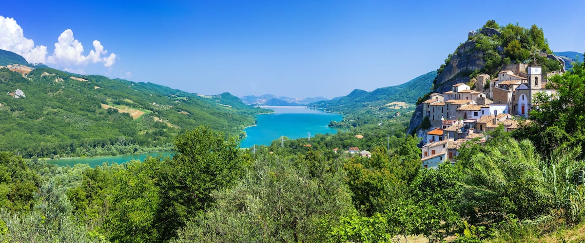 A coastal village with terraced houses, a clear blue sea, and lush green hills.