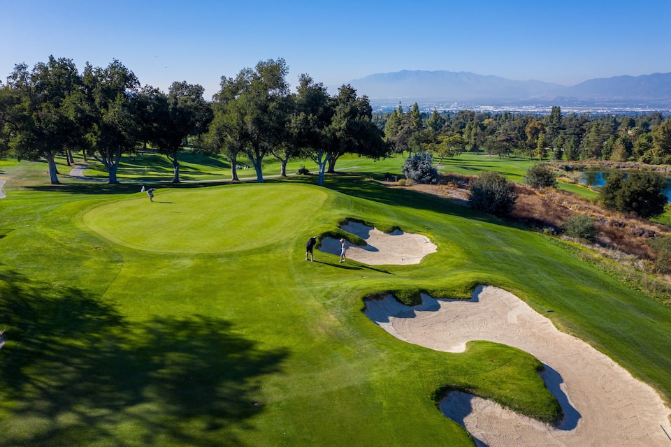 Een golfbaan met zandbunkers, bomen en een heldere blauwe lucht.