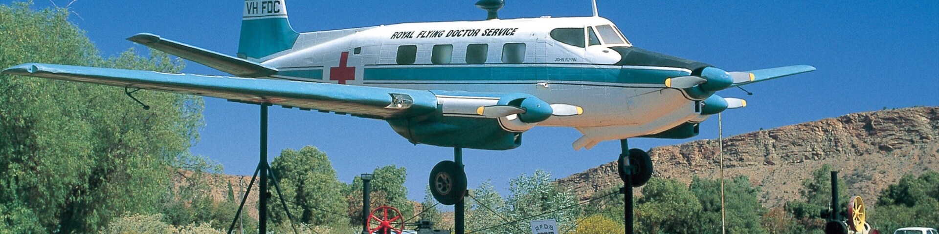 A vintage aircraft with the inscription "Royal Flying Doctor Service" on its side, suspended in an outdoor display.