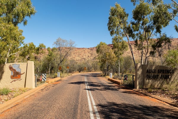 Une route menant au parc désertique d’Alice Springs, avec un paysage désertique et une végétation clairsemée.