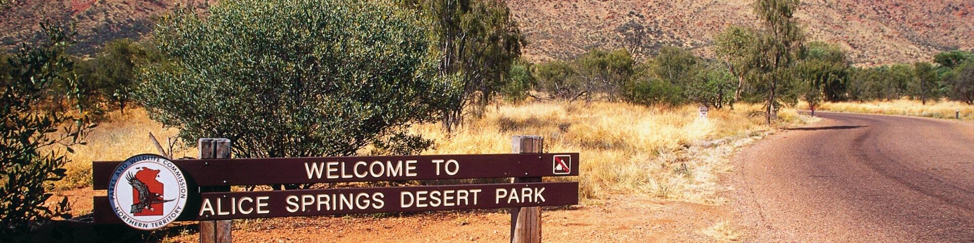 A welcome sign for Alice Springs Desert Park with a red rock mountain in the background.