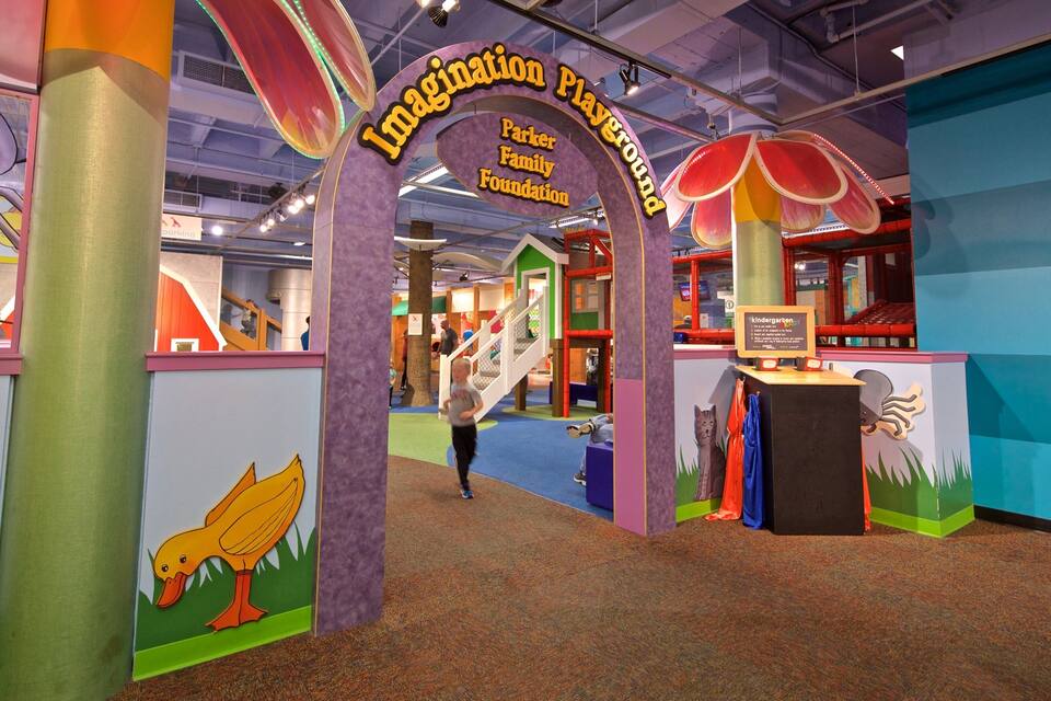 Un área de juegos interior colorida con un cartel que dice 'Imagination Playground' y 'Parker Family Foundation'.