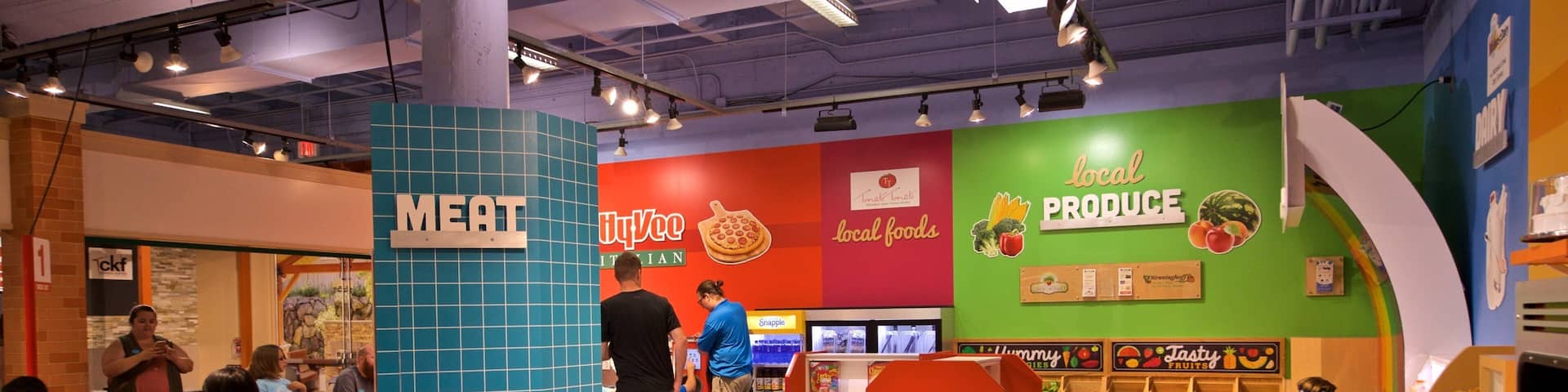 A colorful indoor play area with sections labeled 'MEAT' and 'LOCAL PRODUCE'.