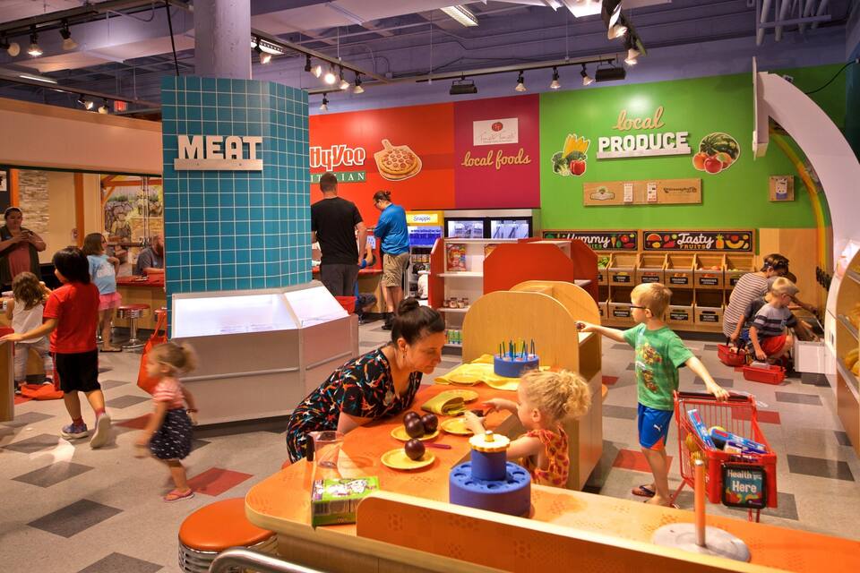 A colorful indoor play area with sections labeled 'MEAT' and 'LOCAL PRODUCE'.