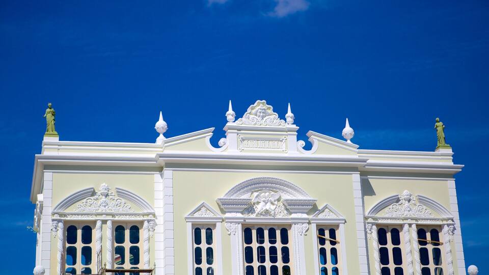 Un edificio imponente con detalles blancos ornamentados, estatuas y un cielo azul despejado al fondo.