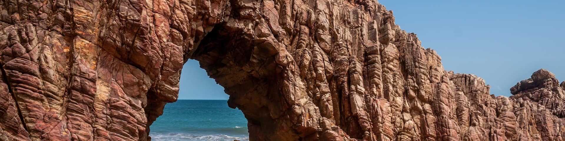 A rocky arch formation on a beach with the ocean in the background.