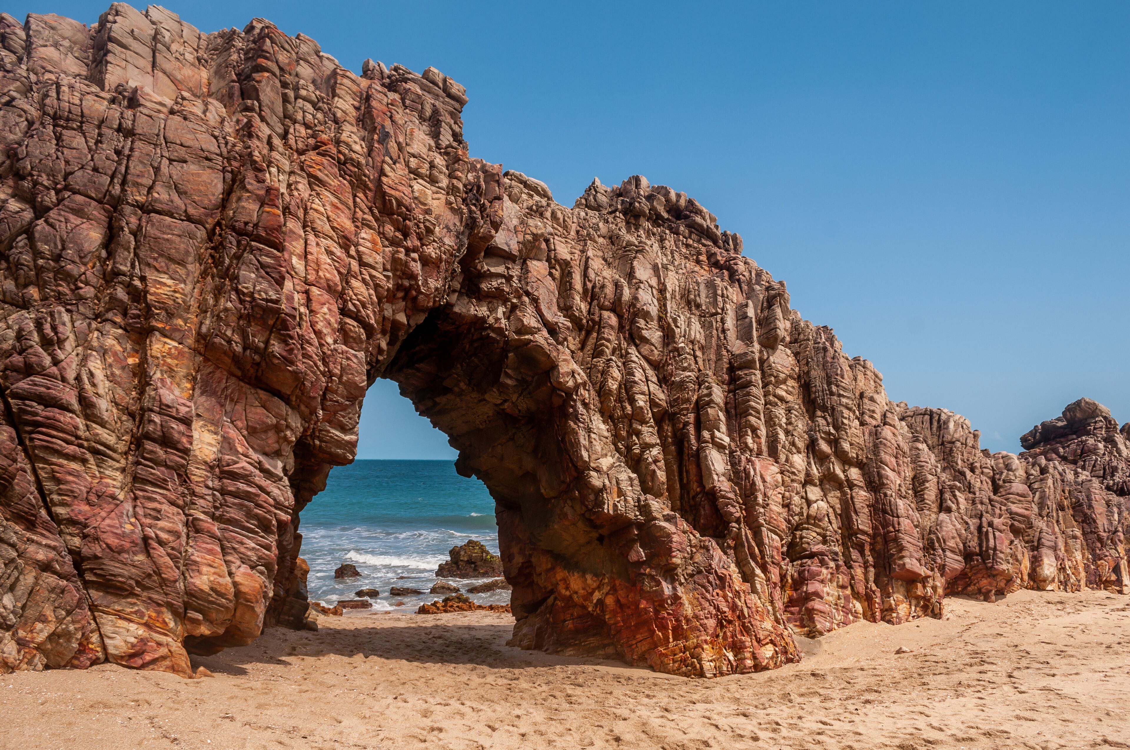 A rocky arch formation on a beach with the ocean in the background.