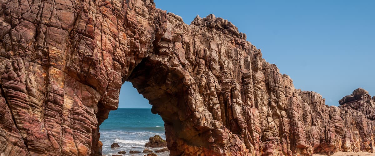A rocky arch formation on a beach with the ocean in the background.