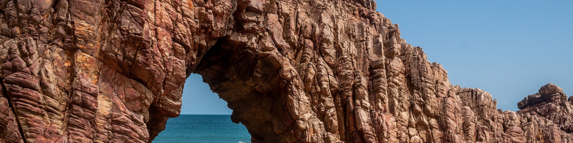 A rocky arch formation on a beach with the ocean in the background.