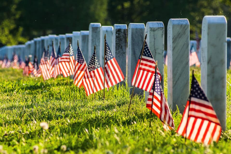 A row of gravestones with American flags planted in the grass.