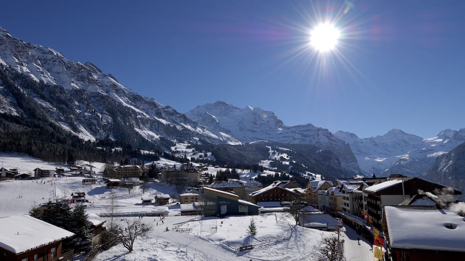 A snow-covered mountain village with buildings and a ski slope.