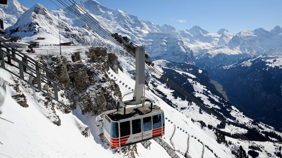 A cable car on a snowy mountain with a clear view of the surrounding peaks.