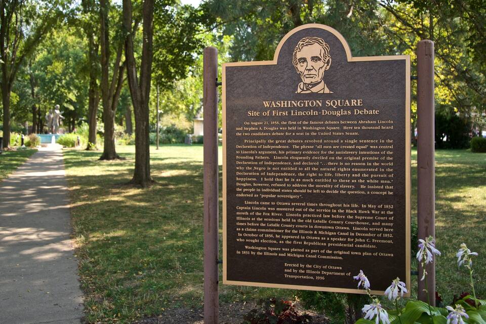 A historical marker in a park with a paved path and trees.