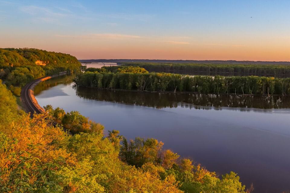 A river curving through a forested landscape with a bridge in the distance.