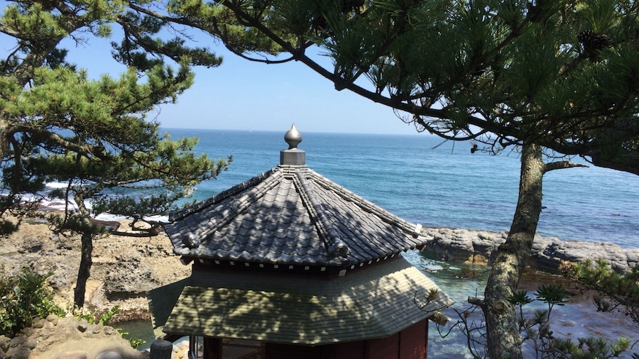 A traditional Japanese pavilion with a tiled roof overlooking the sea.