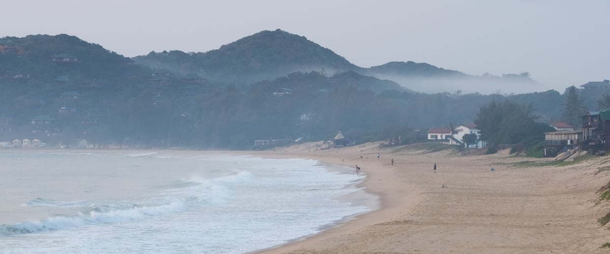 A beach with waves, a sandy shore, and buildings on the hillside.