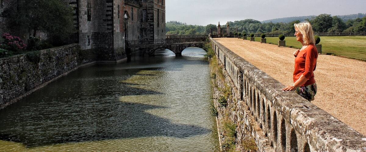 A historic building with a moat and a bridge, overlooking a river.