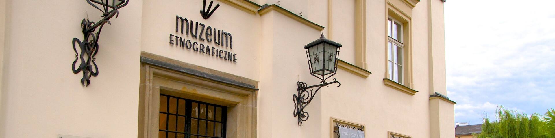 The entrance to the Muzeum Etnograficzne with a metal gate, a signboard, and a street lamp.