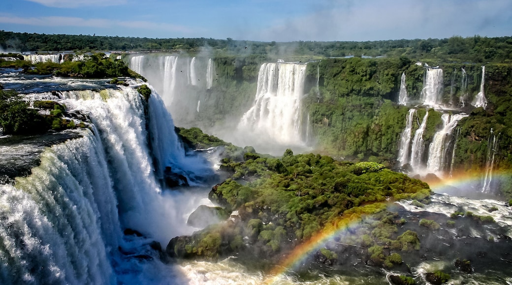 Water cascading over the Iguacu falls with rainbow in foreground in Brazil
